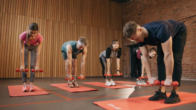 Adults exercising in an indoor fitness class with dumbbells and yoga mats for healthy lifestyle.